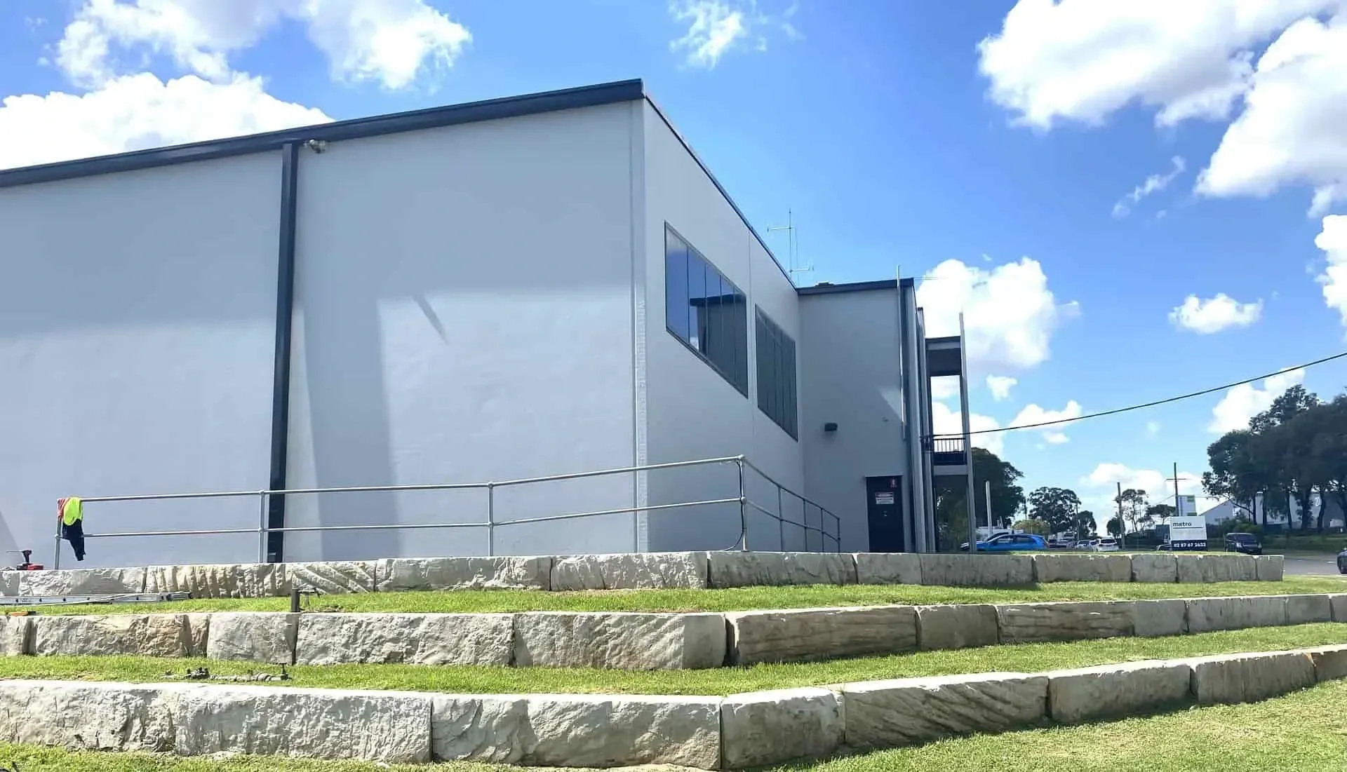 A modern, gray building with stone terraced steps in the foreground under a blue sky with white clouds.