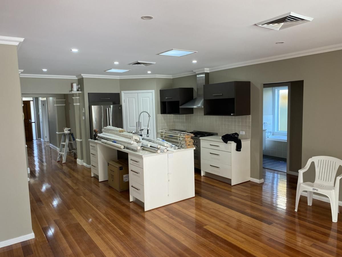 Modern kitchen with white island, dark cabinetry, and wood floors, featuring a white plastic chair in the corner.