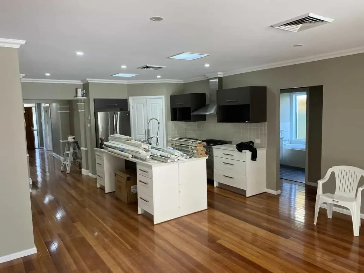Open-plan kitchen with wood floors, white cabinets, a central island, and dark upper cabinets in a brightly lit room.