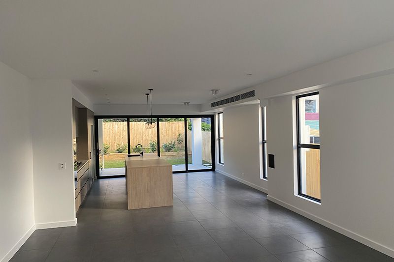 A modern, minimalist kitchen and living space with grey tile floors, white walls, and floor-to-ceiling glass doors.