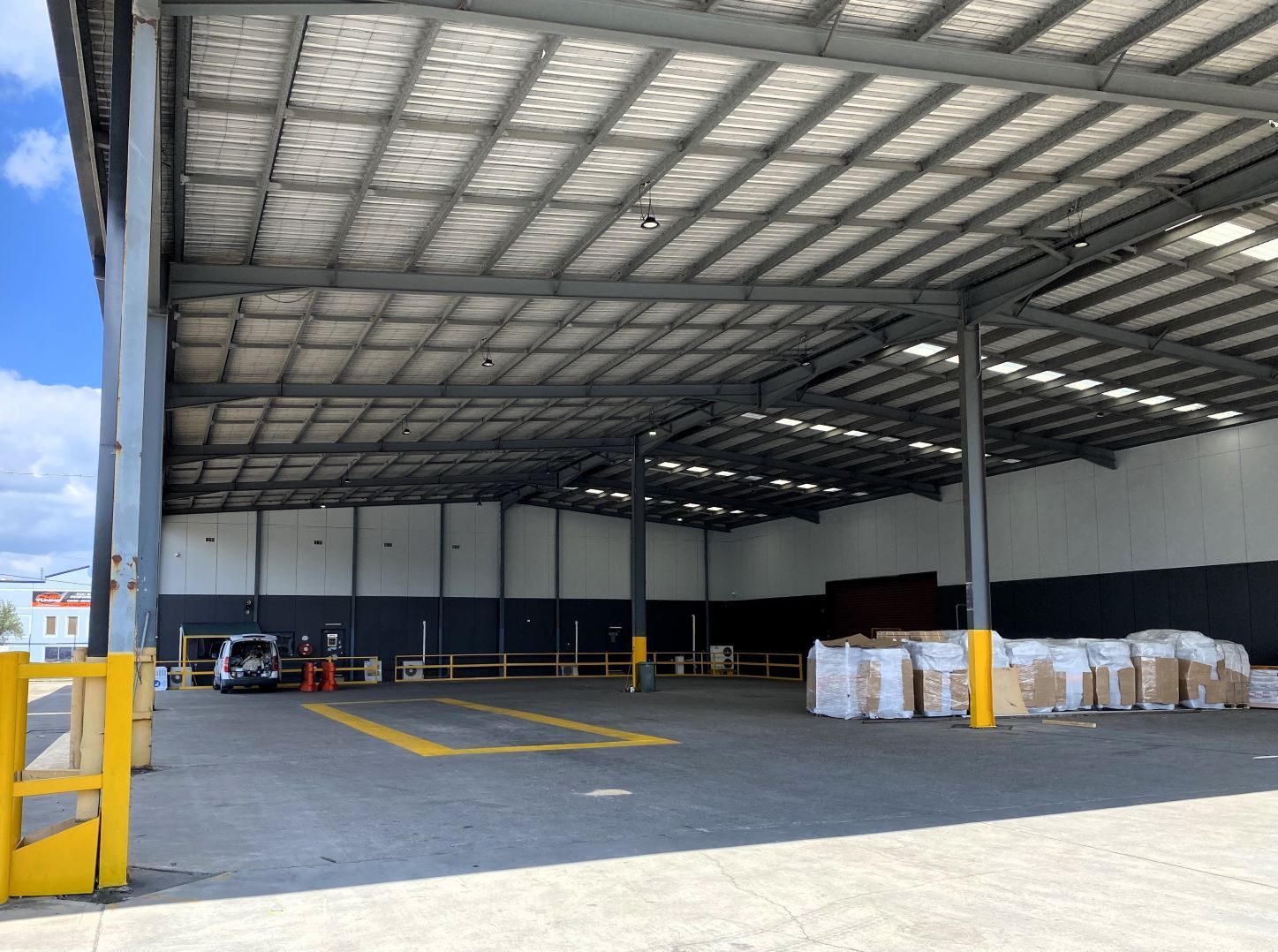 A large, open-air warehouse loading dock with gray metal framing, a white roof, and stacked white shipping pallets.
