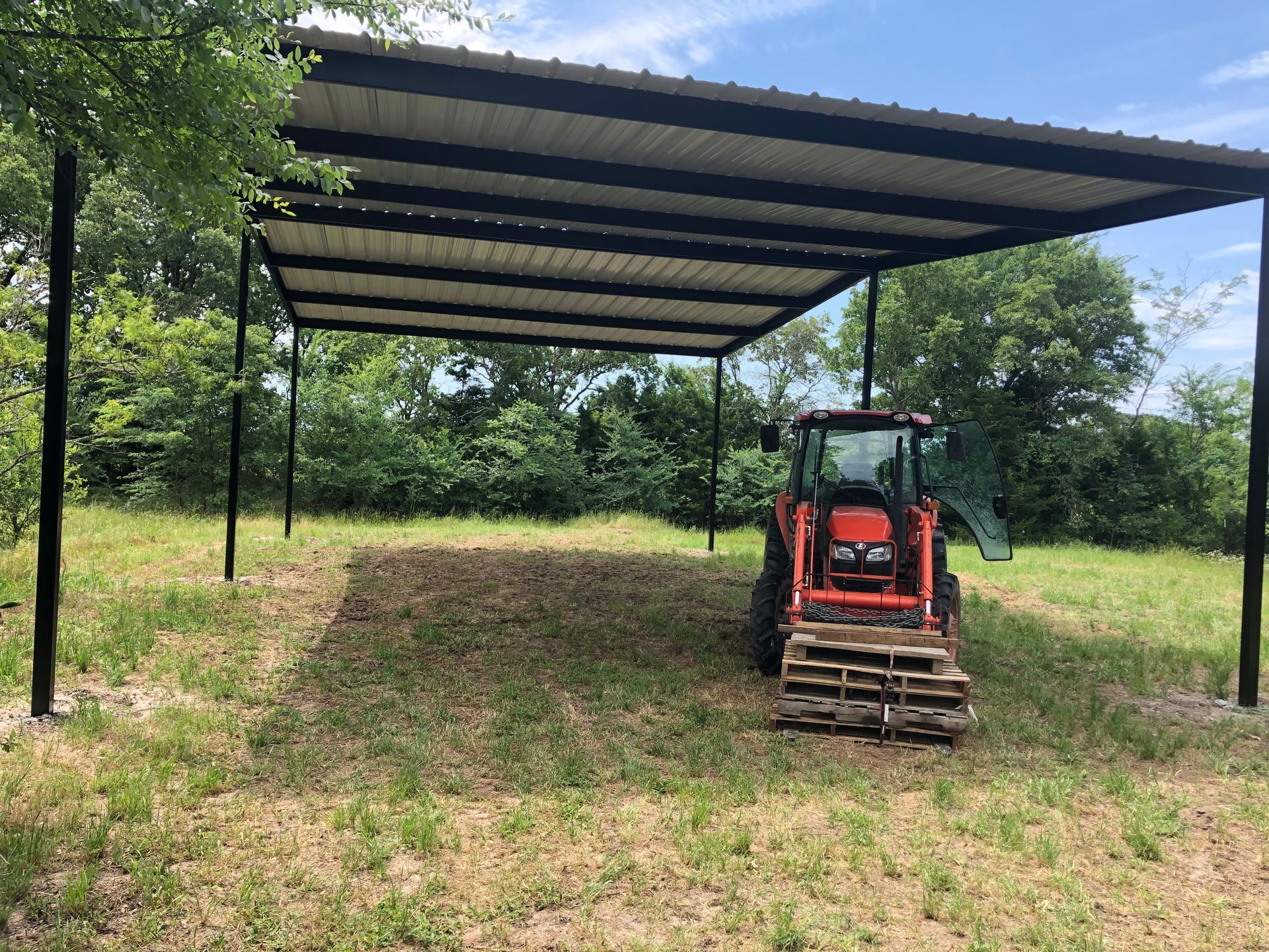 A tractor is parked under a metal roof in a field.