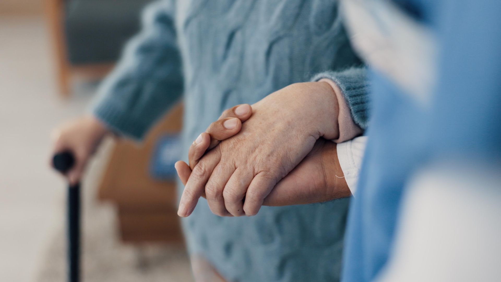 A nurse is holding the hand of an elderly woman with a cane.