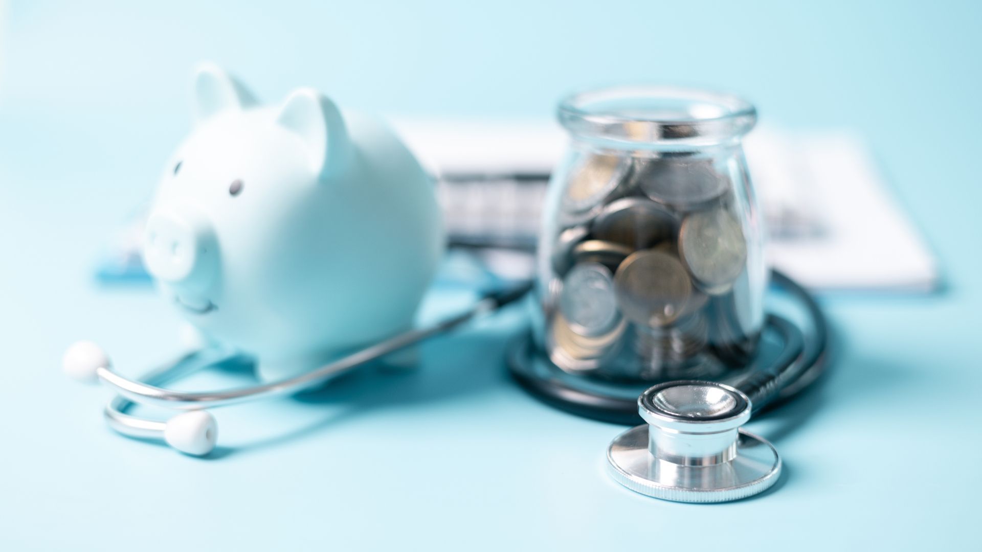 A piggy bank , stethoscope and jar of coins on a blue background.