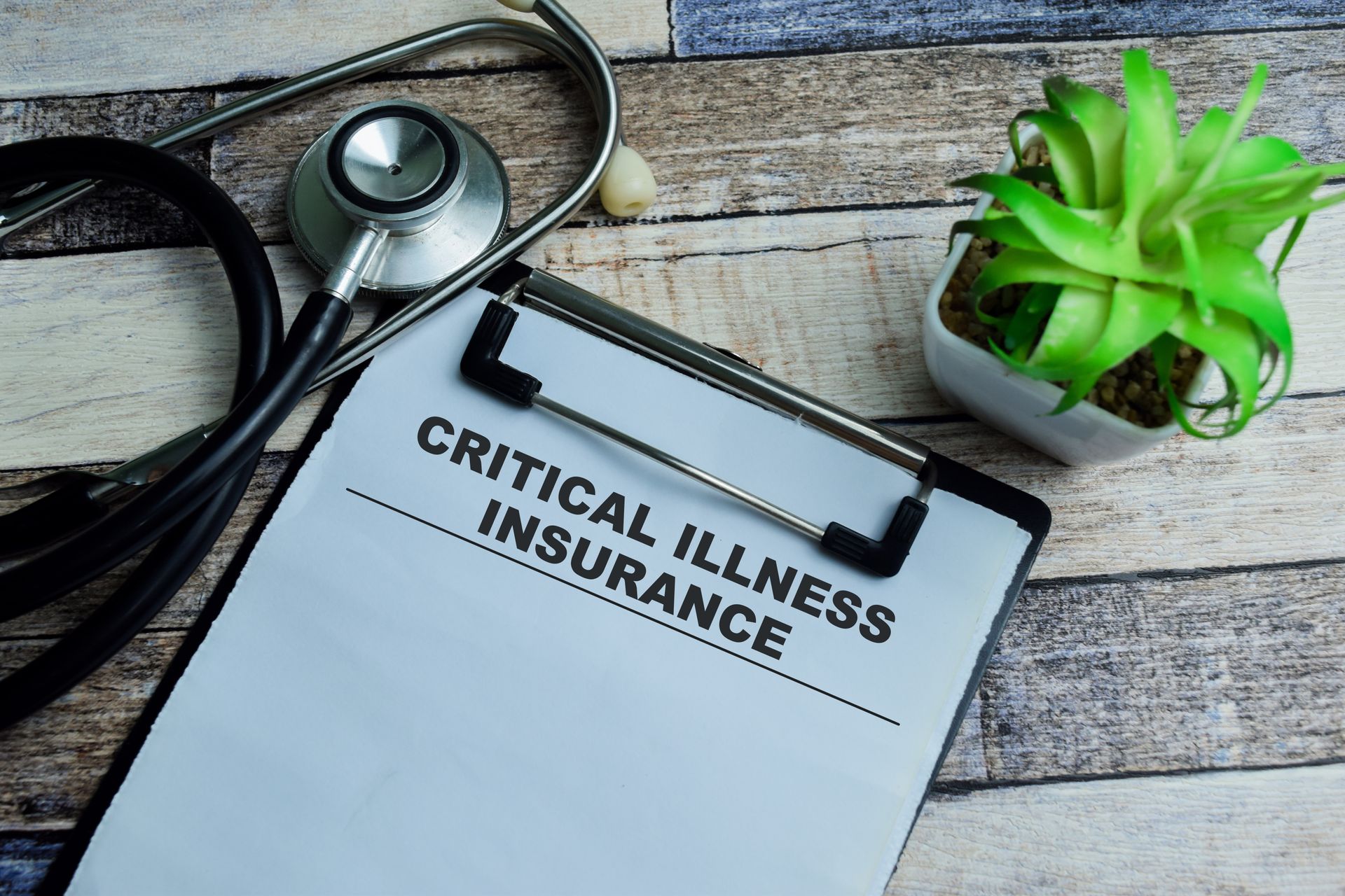 A clipboard with the words `` critical illness insurance '' written on it next to a stethoscope and a plant.