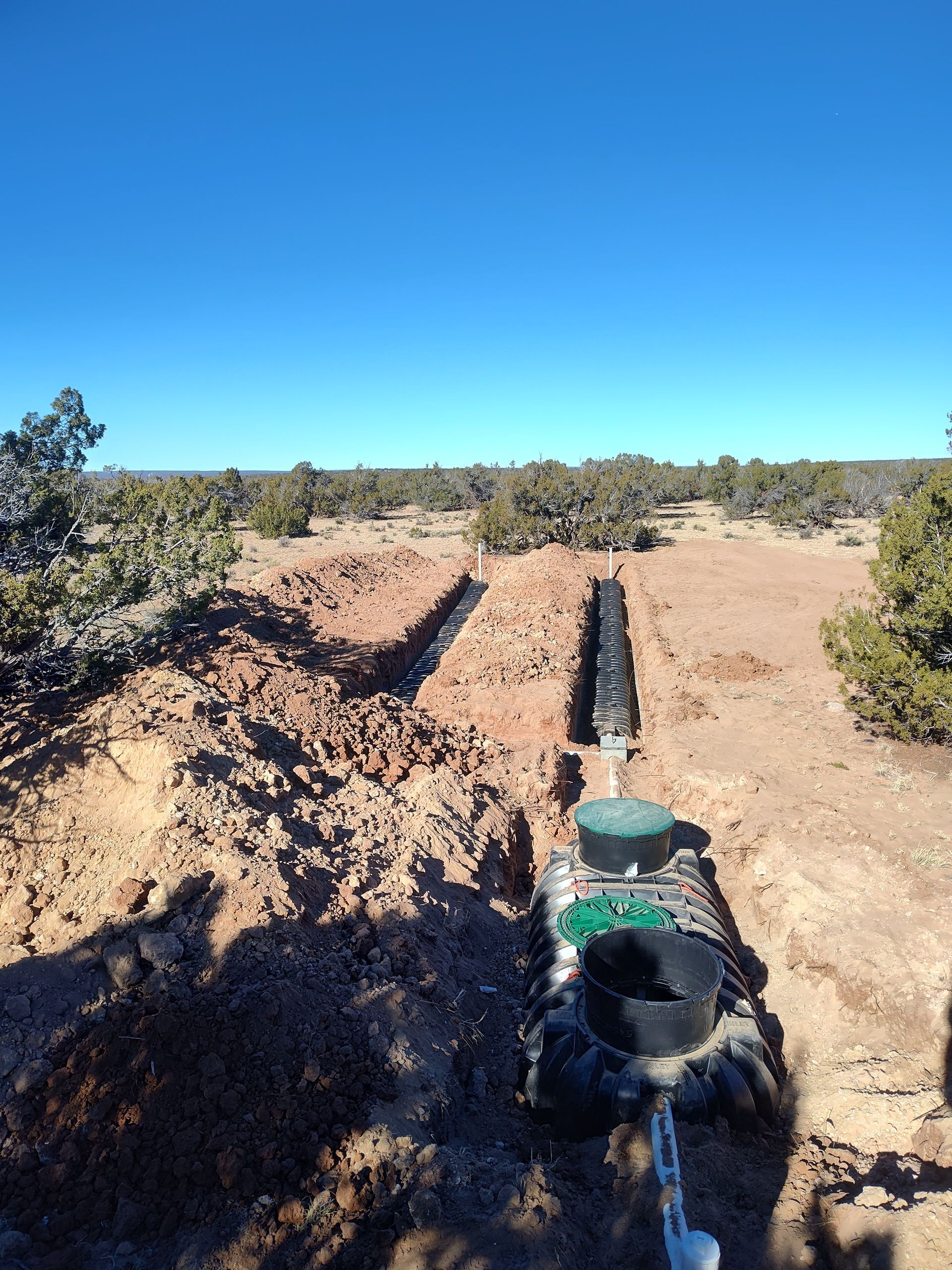 Excavator trenching in a dry, dirt field under a clear blue sky