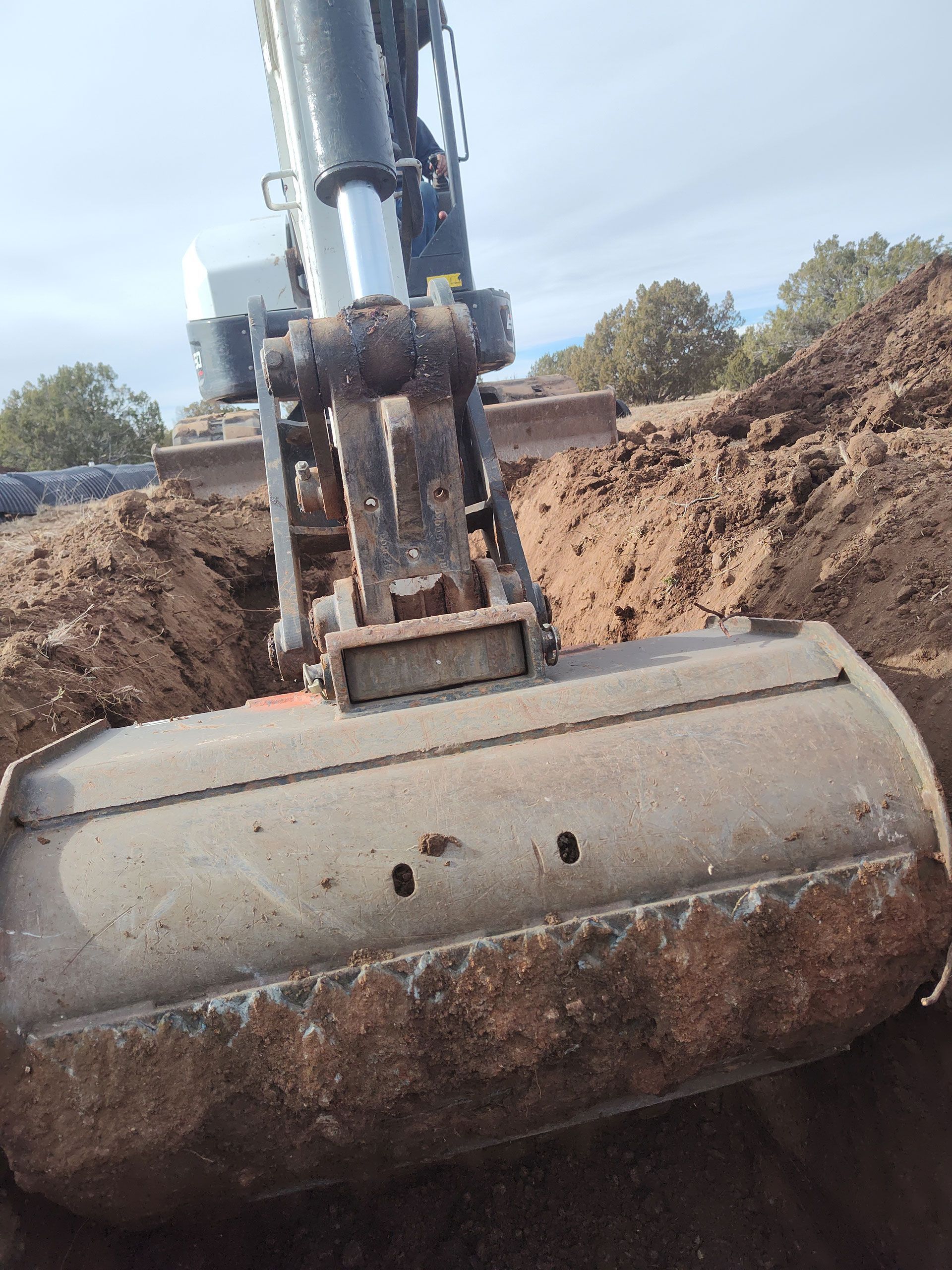 Excavator bucket lifting a mud-covered cylindrical tank at a muddy construction site