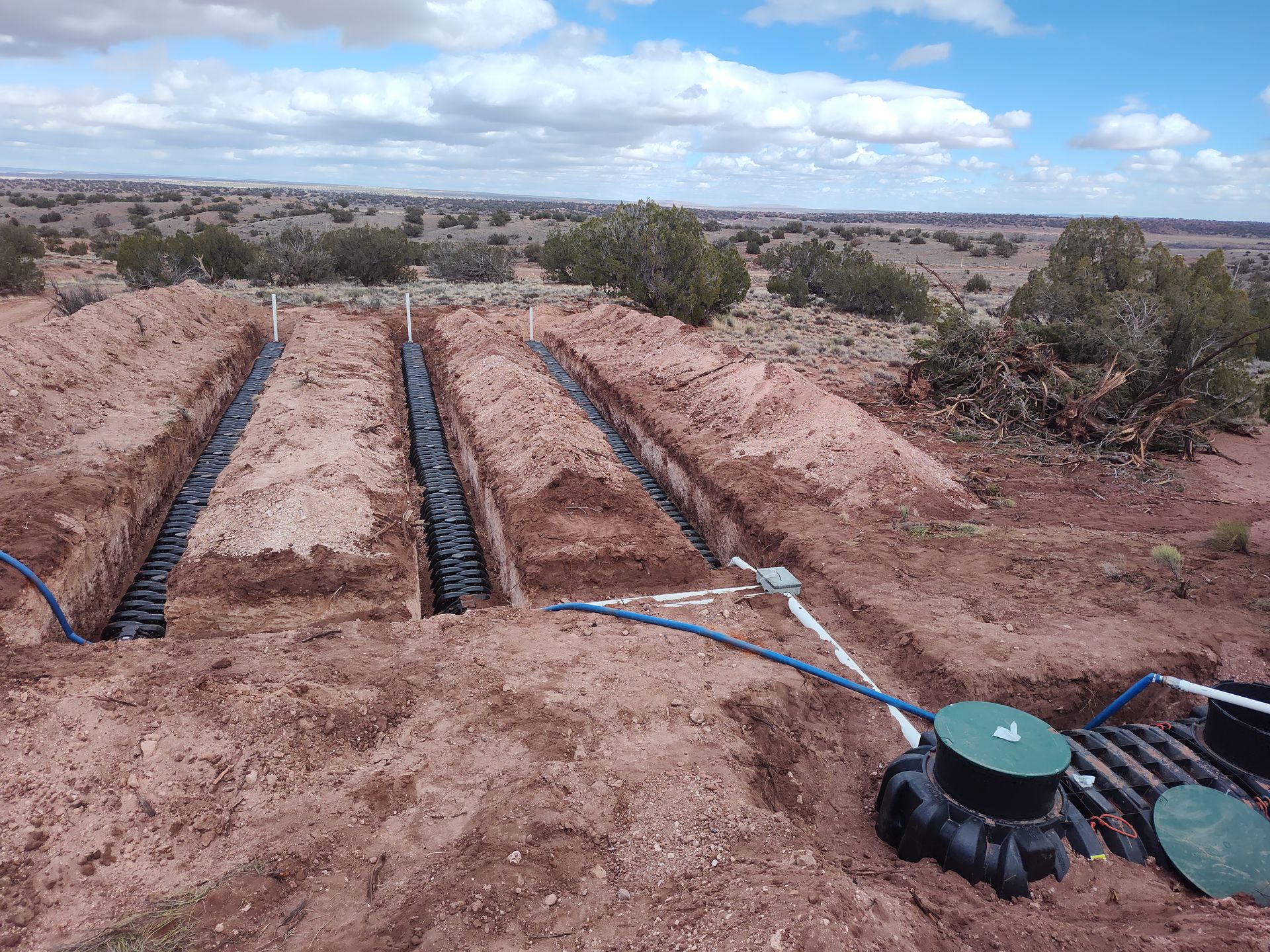 Irrigation trenches with black pipes in a dry dirt field, with blue tubing and green valve covers.
