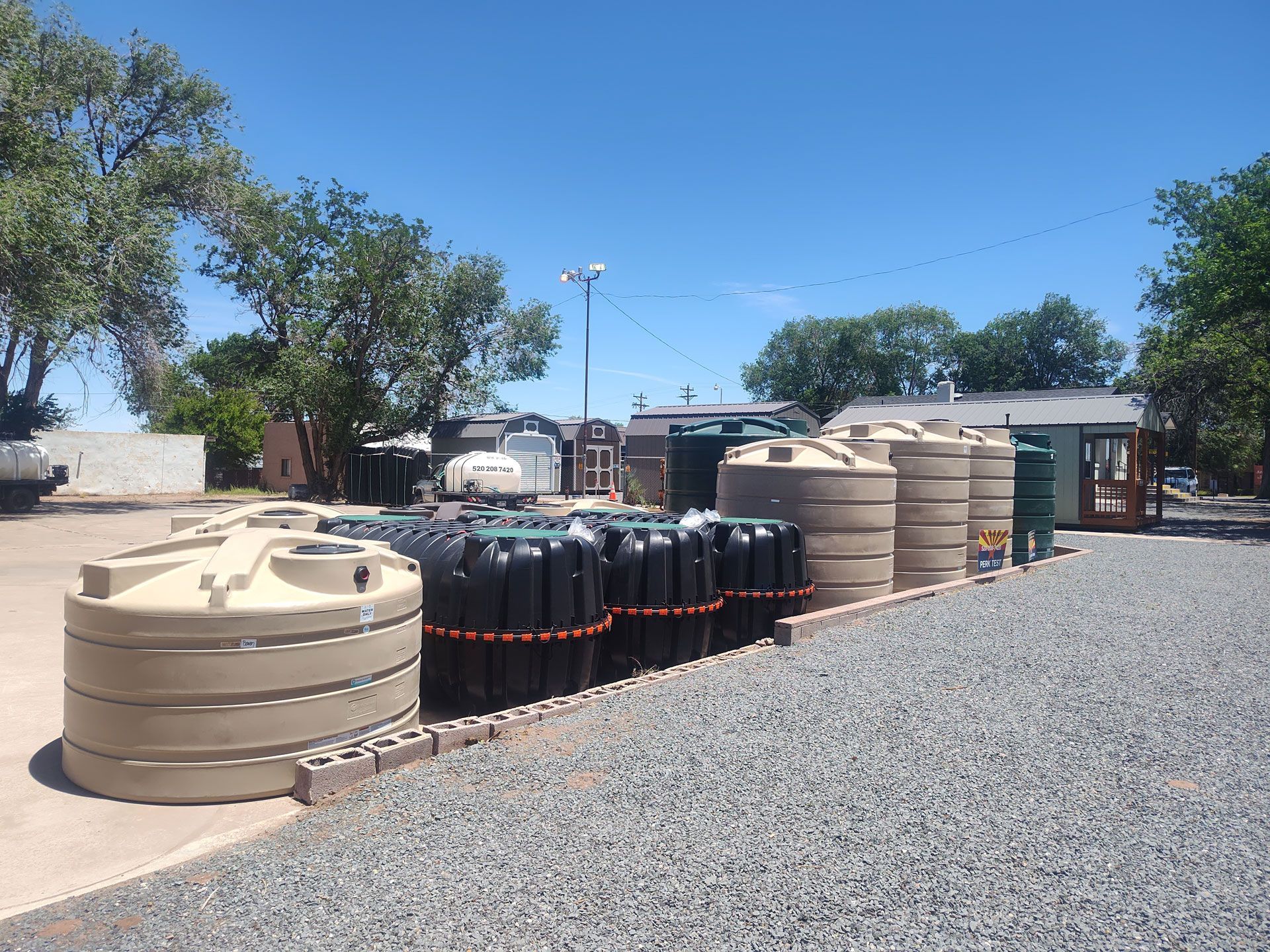 Stacked industrial pipes and tanks in a gravel yard under a clear blue sky