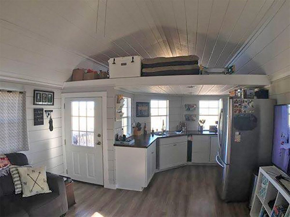 Bright living room with a kitchen, gray sofa, tall fridge, and vaulted ceiling light lines