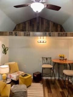 Cozy attic sitting area with wood floor, ceiling fan, small table, stools, and warm wall lighting