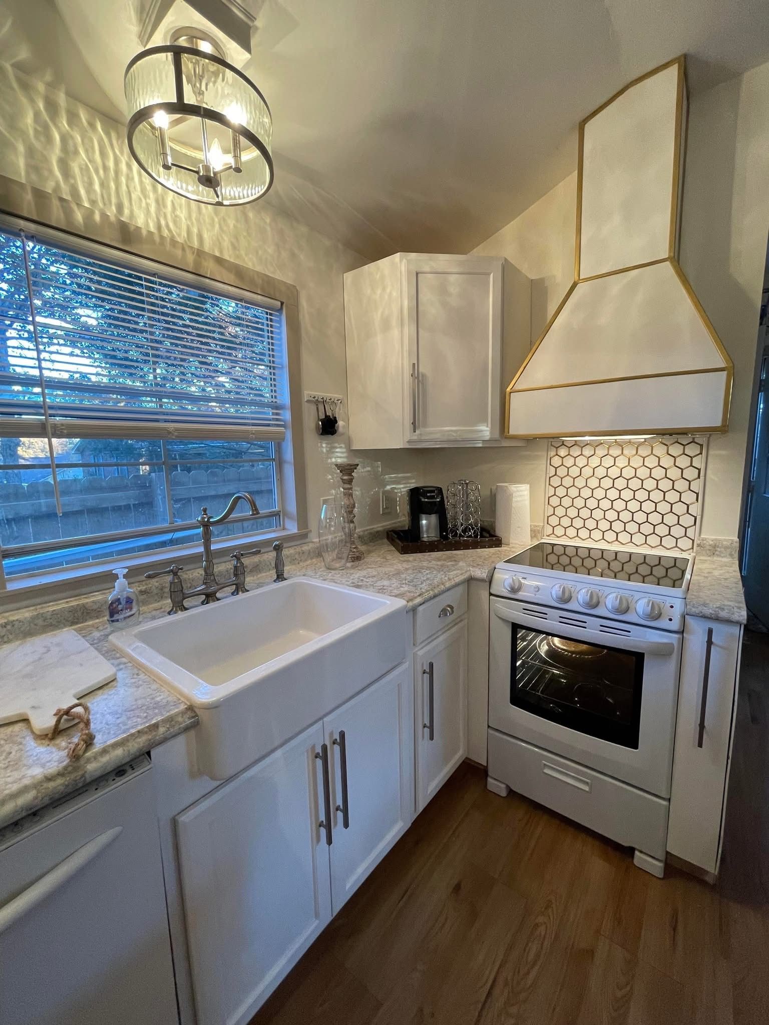 Bright white kitchen with farmhouse sink, stove, cabinets, and window above the counter.