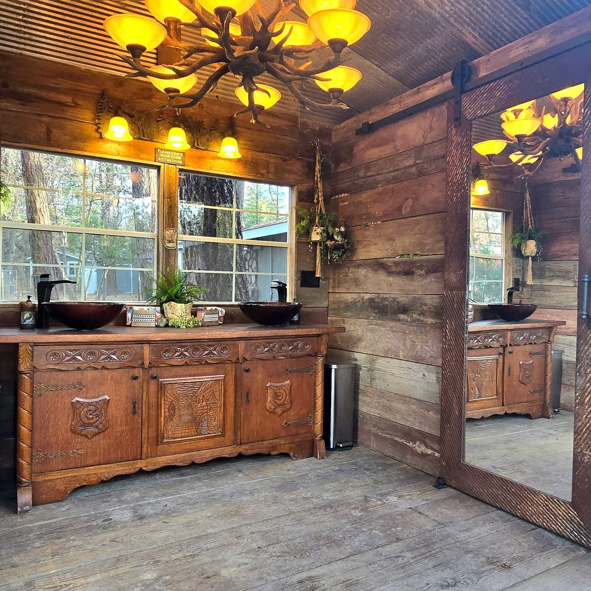 Rustic bathroom with carved wood vanity, twin sinks, large mirror, and warm yellow lighting