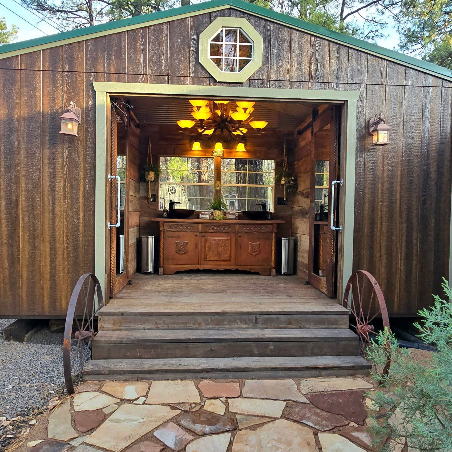 Rustic brown barn-style outbuilding with open front, wagon wheels, and a wooden cabinet inside.