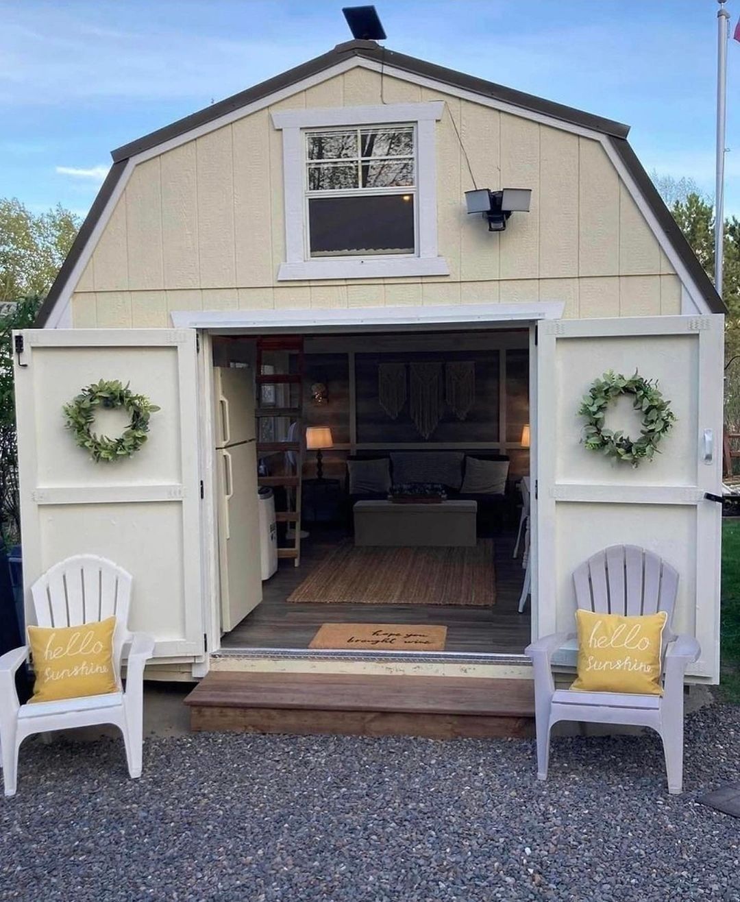 Open white beach cottage with wreaths, yellow chairs, and a view into a cozy interior.