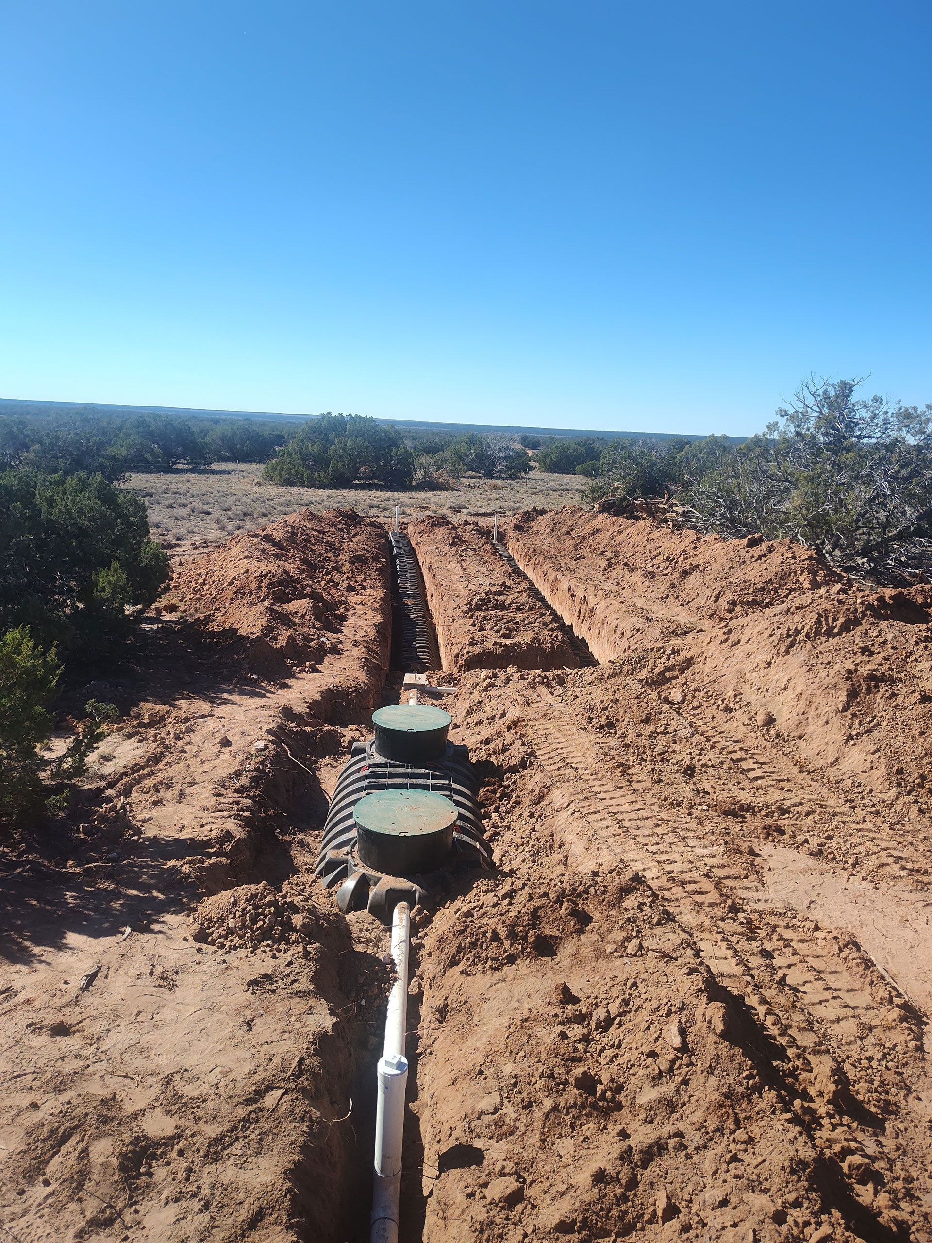 Excavator bucket lifting a mud-covered cylindrical tank at a muddy construction site
