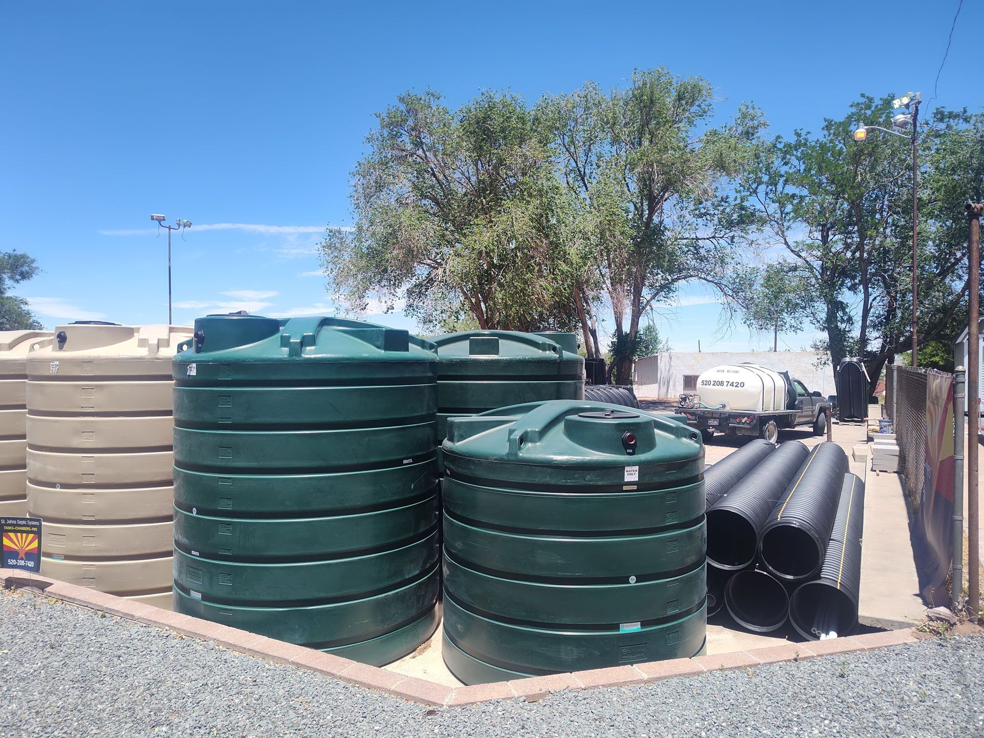 Stacks of green and beige water tanks and black pipes outdoors under a clear blue sky