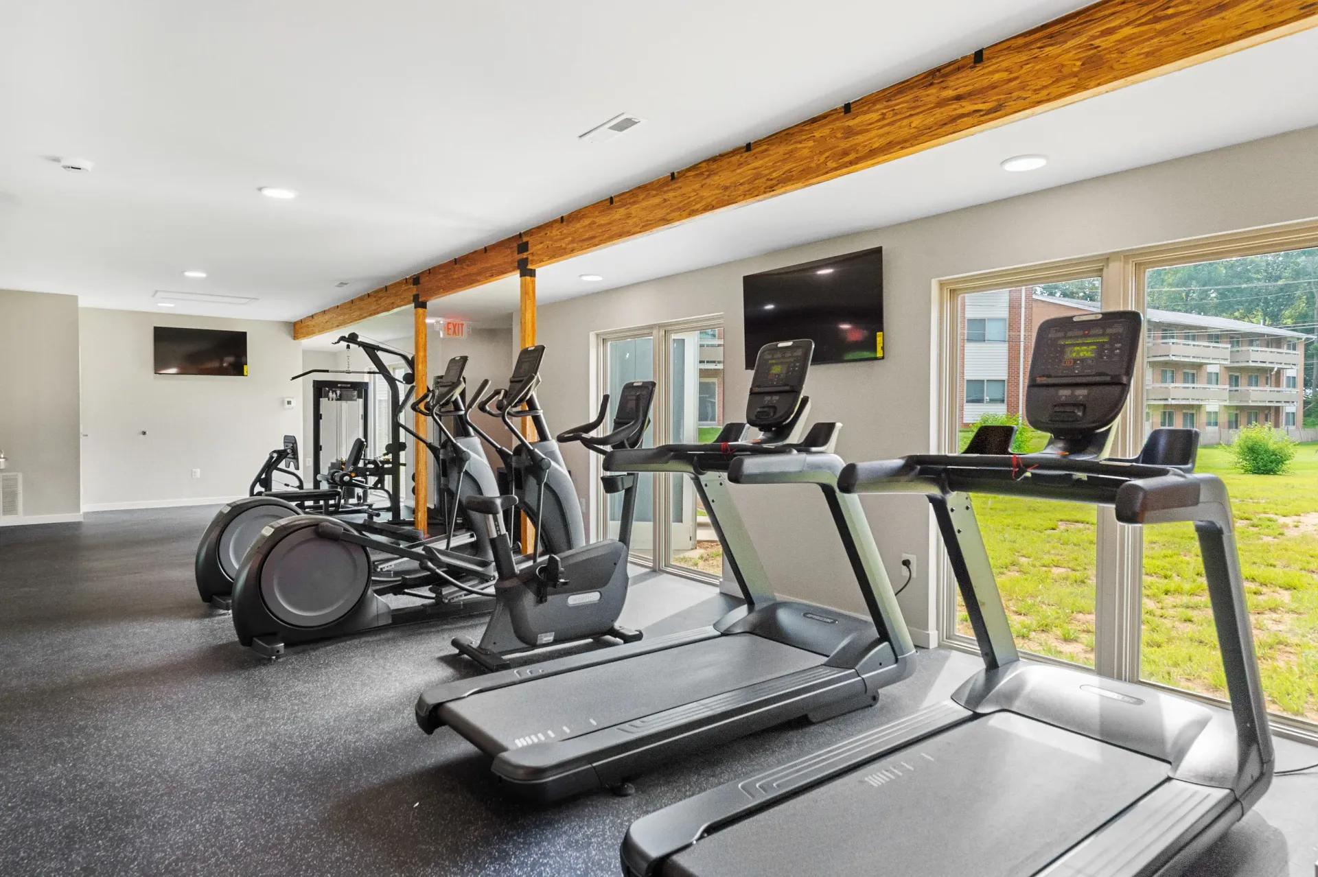 Indoor fitness center with treadmills, ellipticals, and a wall-mounted TV by large windows at The Ridge Apartments in Hagerstown, MD