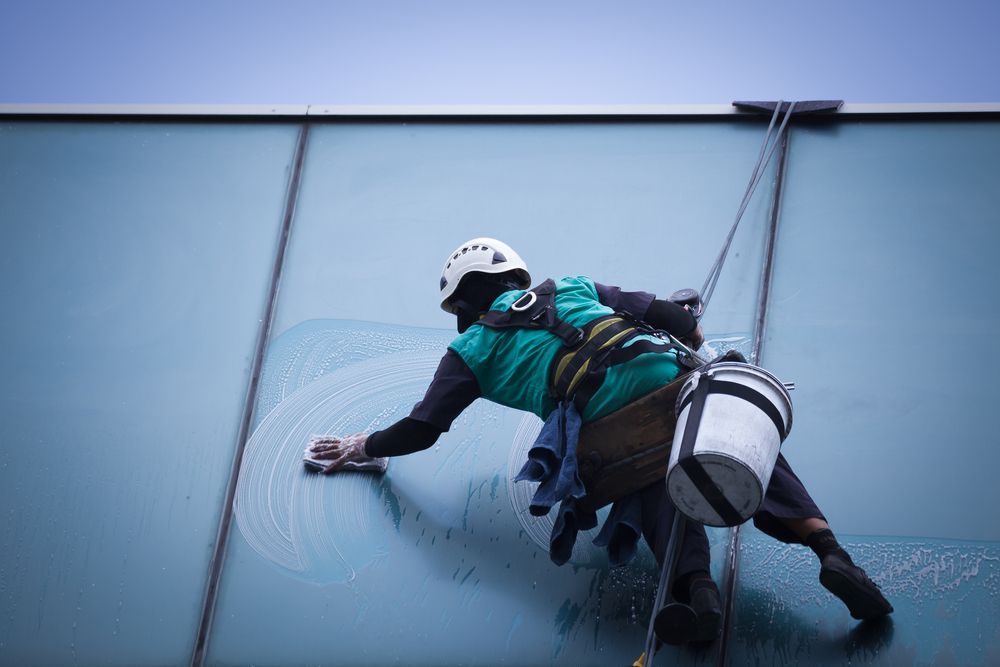 A Man is Cleaning a Building With a Bucket and a Mop — Dazzling Windows & Pressure Cleaning in Tugun, QLD