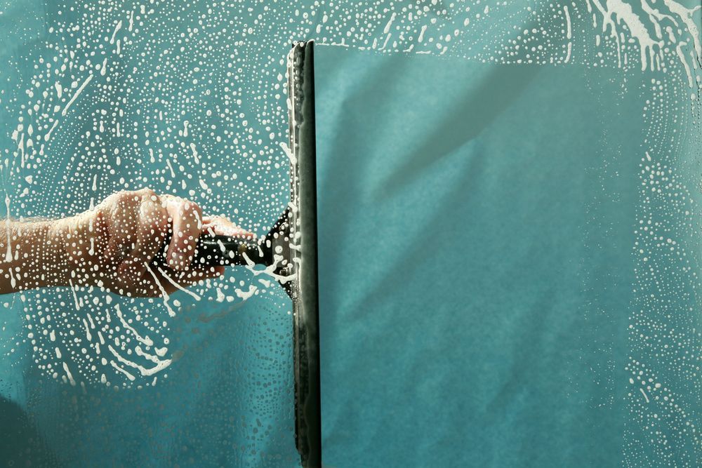 A Person is Cleaning a Window With a Squeegee — Dazzling Windows & Pressure Cleaning in Coolangatta, QLD