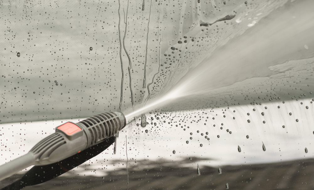 Pressure washer spraying a soapy window covered in water droplets.