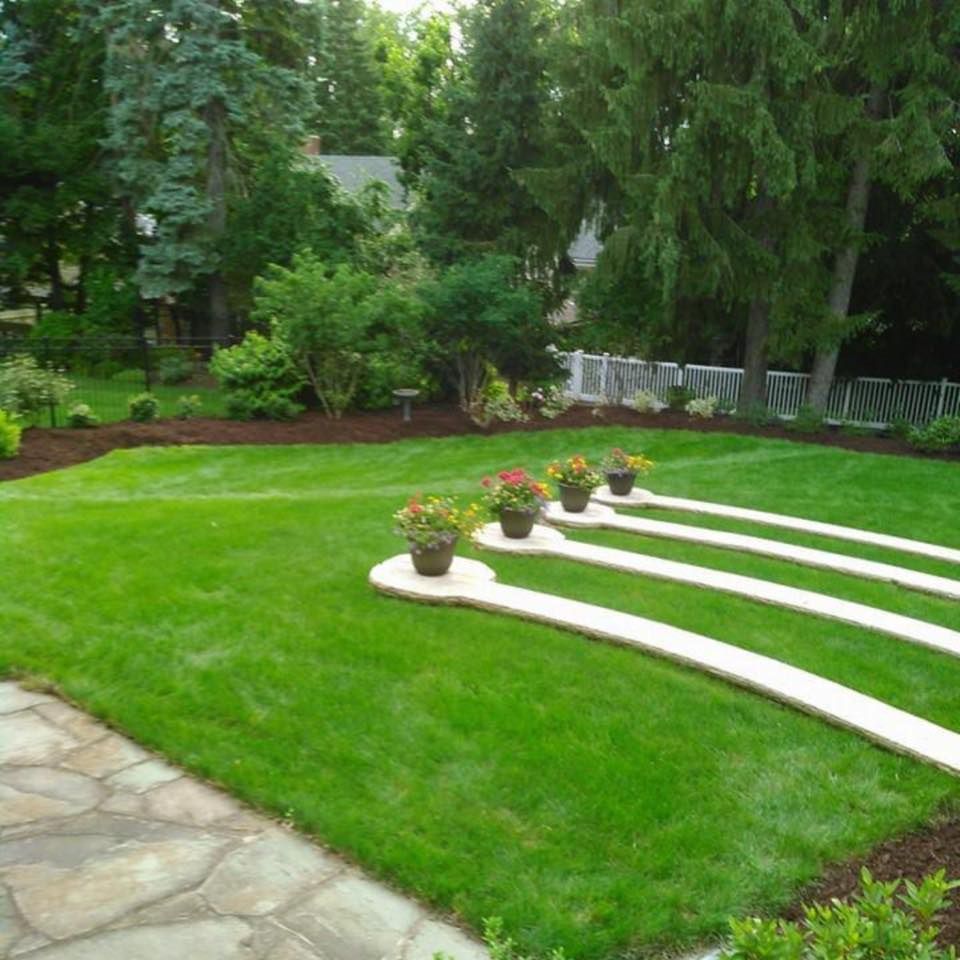 Lush green backyard with a stone patio, curving walkways, and potted flowers.