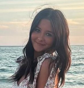 A young woman is standing on the beach smiling at the camera.