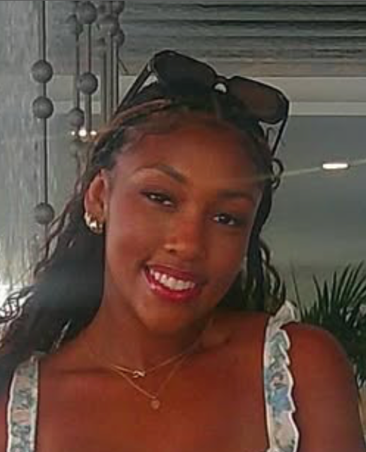 A woman wearing sunglasses and a necklace is smiling for the camera.