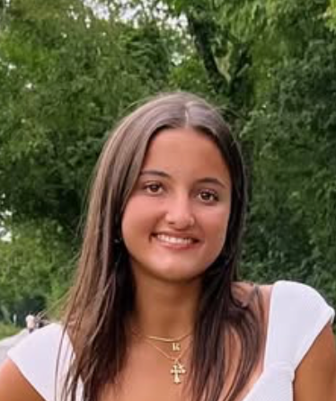 A young woman wearing a white shirt and a cross necklace is smiling for the camera.