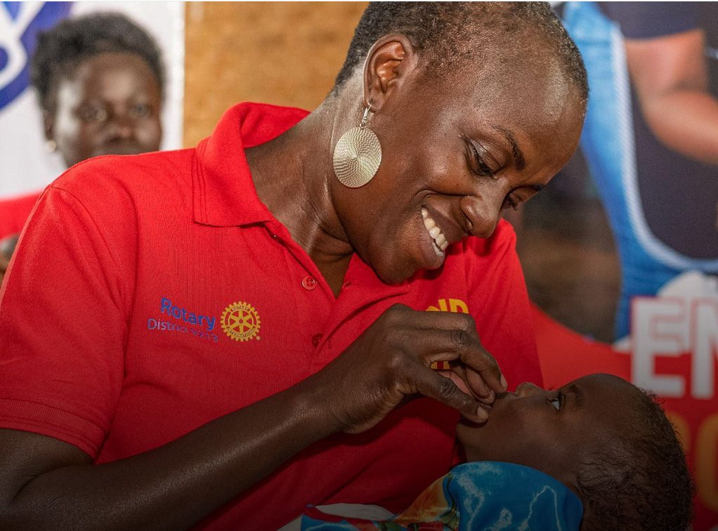 Woman in red shirt administering oral medication to a child.