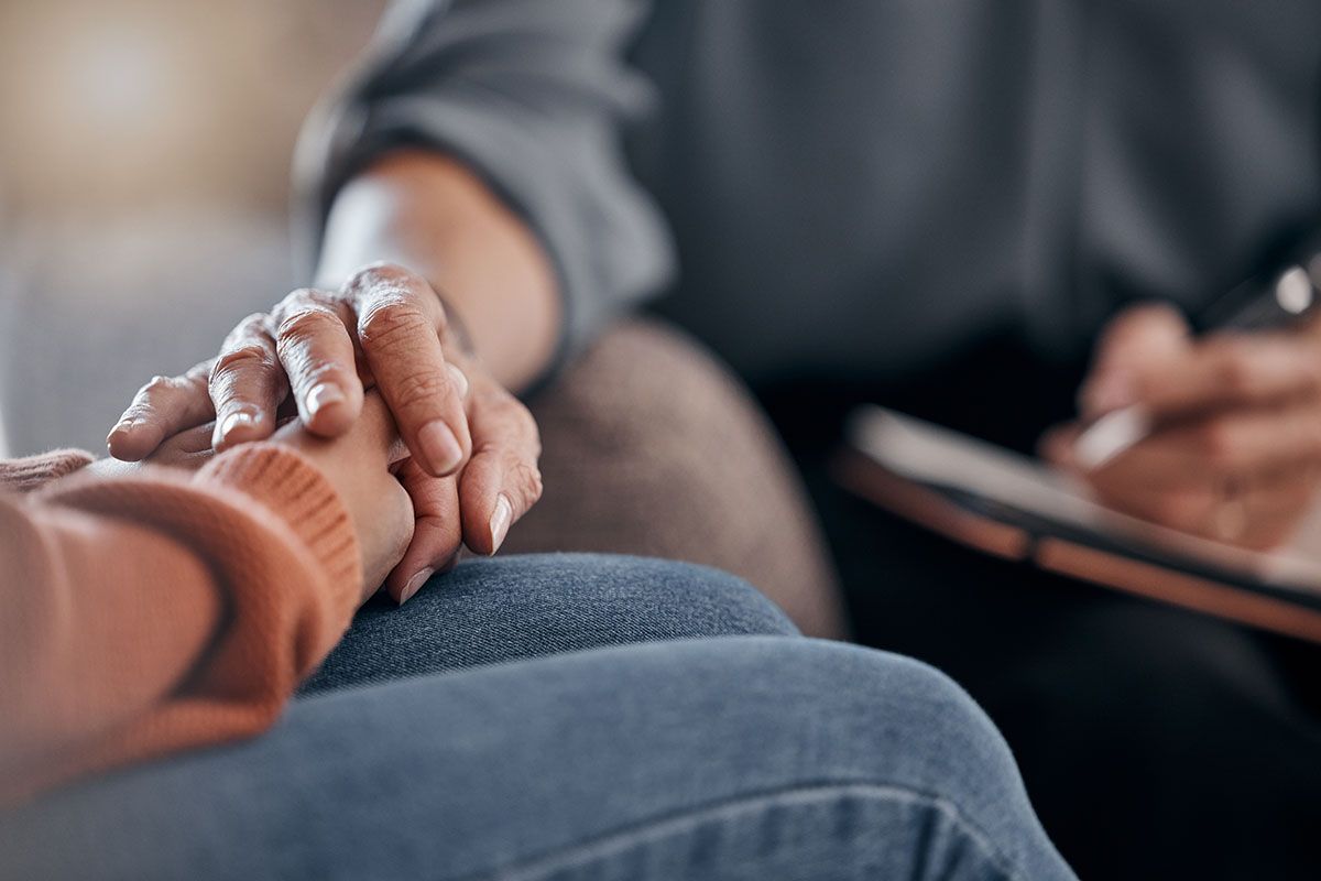 A man and a woman are holding hands against a tree trunk.