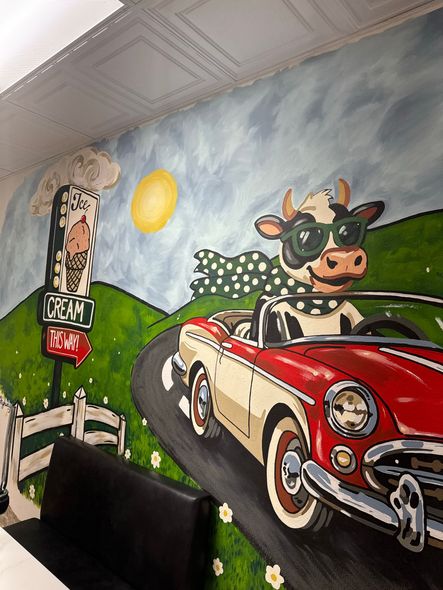 Mural of a cow driving a red vintage car on a winding road with green hills and a sunny sky