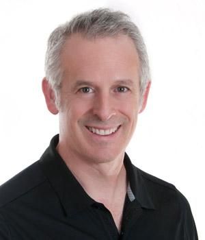 Middle-aged man with graying hair smiles in a black polo shirt against a white background.