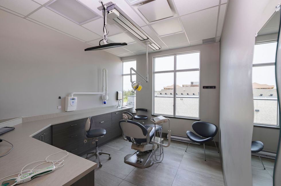 Dental office with dental chair, window, cabinets, and a patient chair.