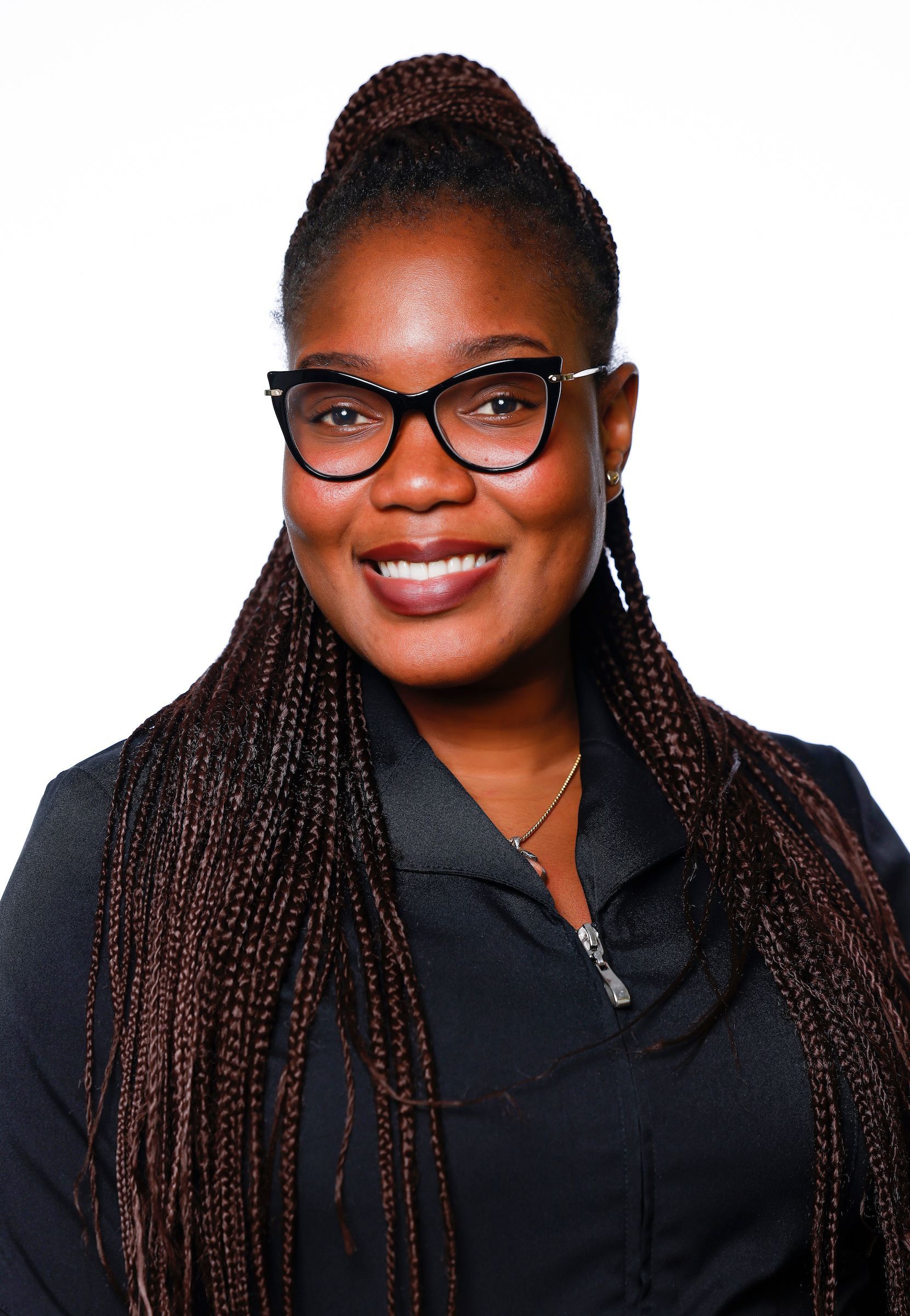 Femme à la peau foncée, portant des lunettes et des cheveux tressés, souriante. Elle porte un blazer foncé sur fond blanc.