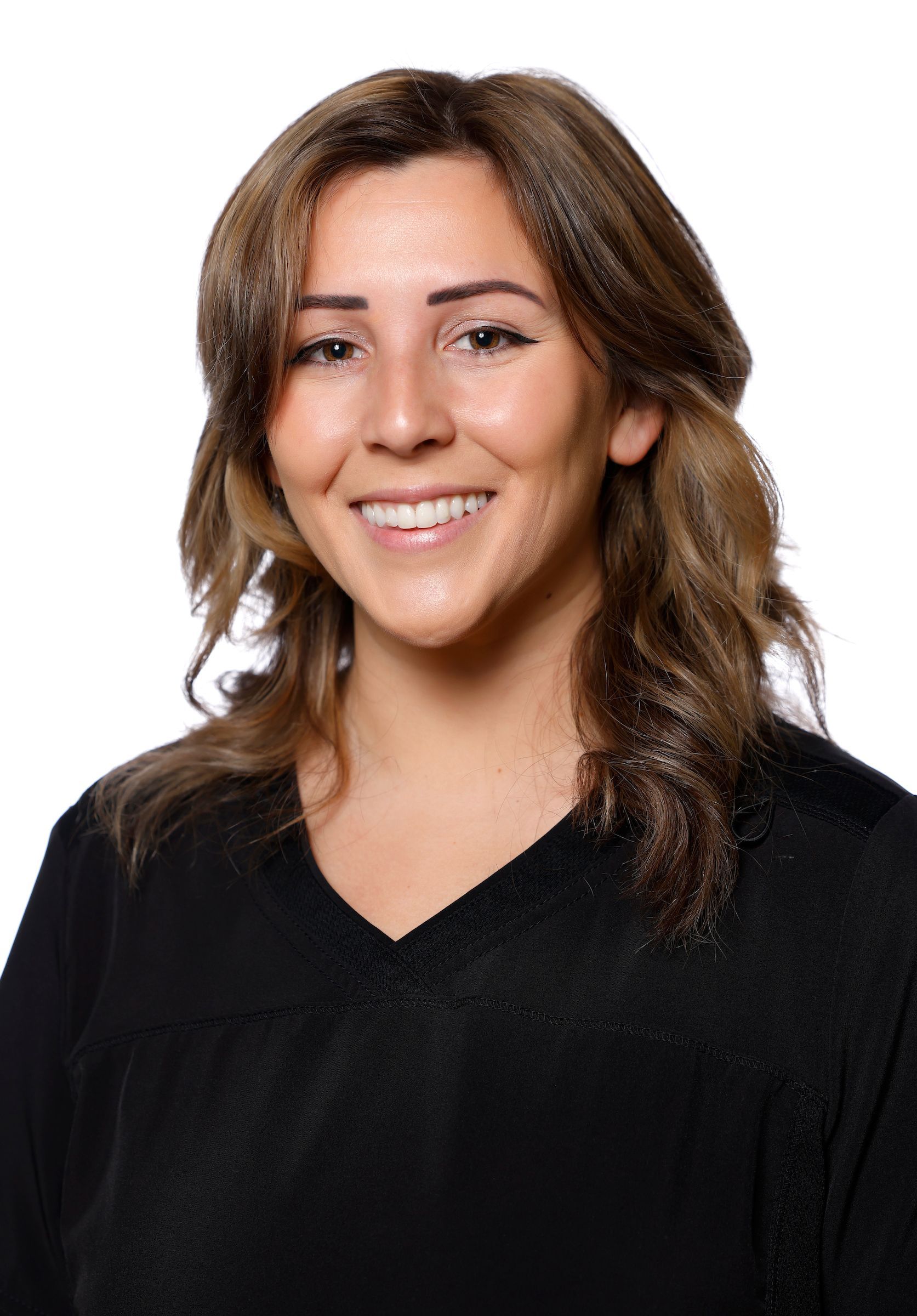 Femme aux cheveux bruns souriante, portant une chemise noire à col en V, fond blanc.