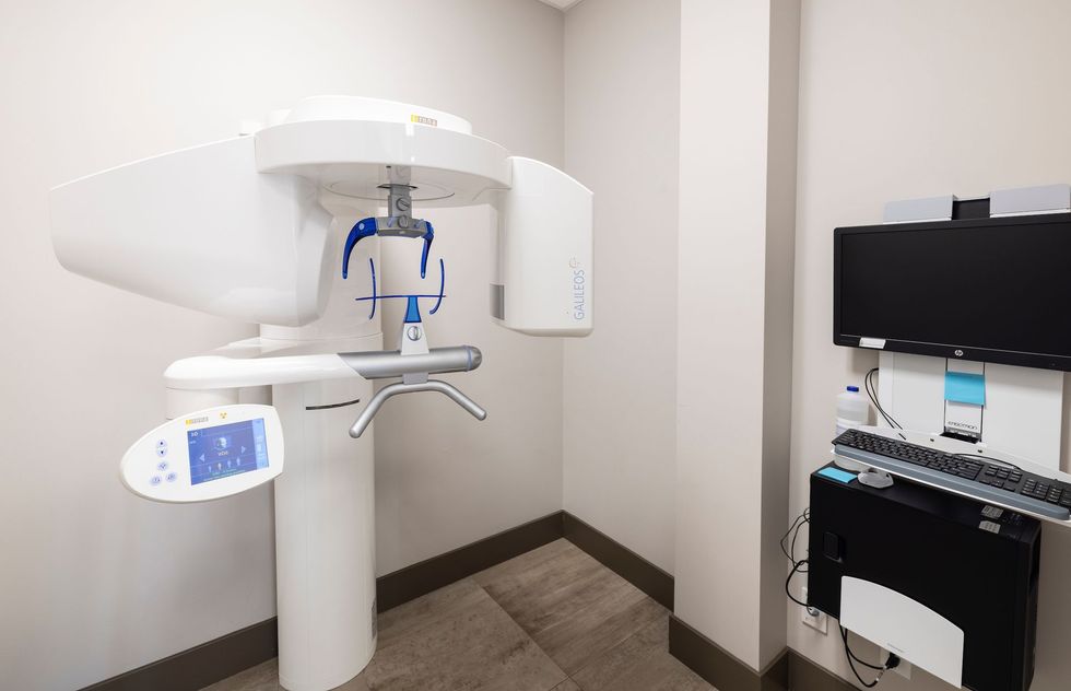 Dental panoramic X-ray machine in a dentist's office with a computer and monitor.
