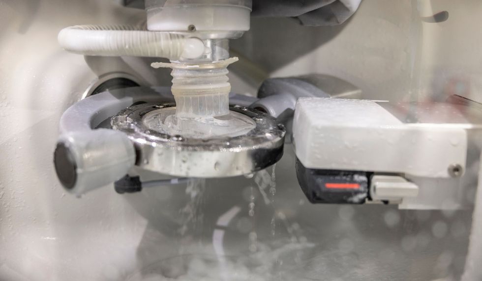 A dental milling machine, spraying water, fabricating a crown in a laboratory setting.