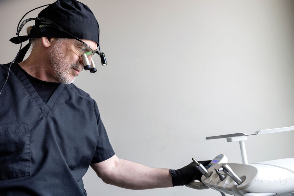Dentist in black scrubs, examining dental tools. Wearing a headlamp, in a dental office.