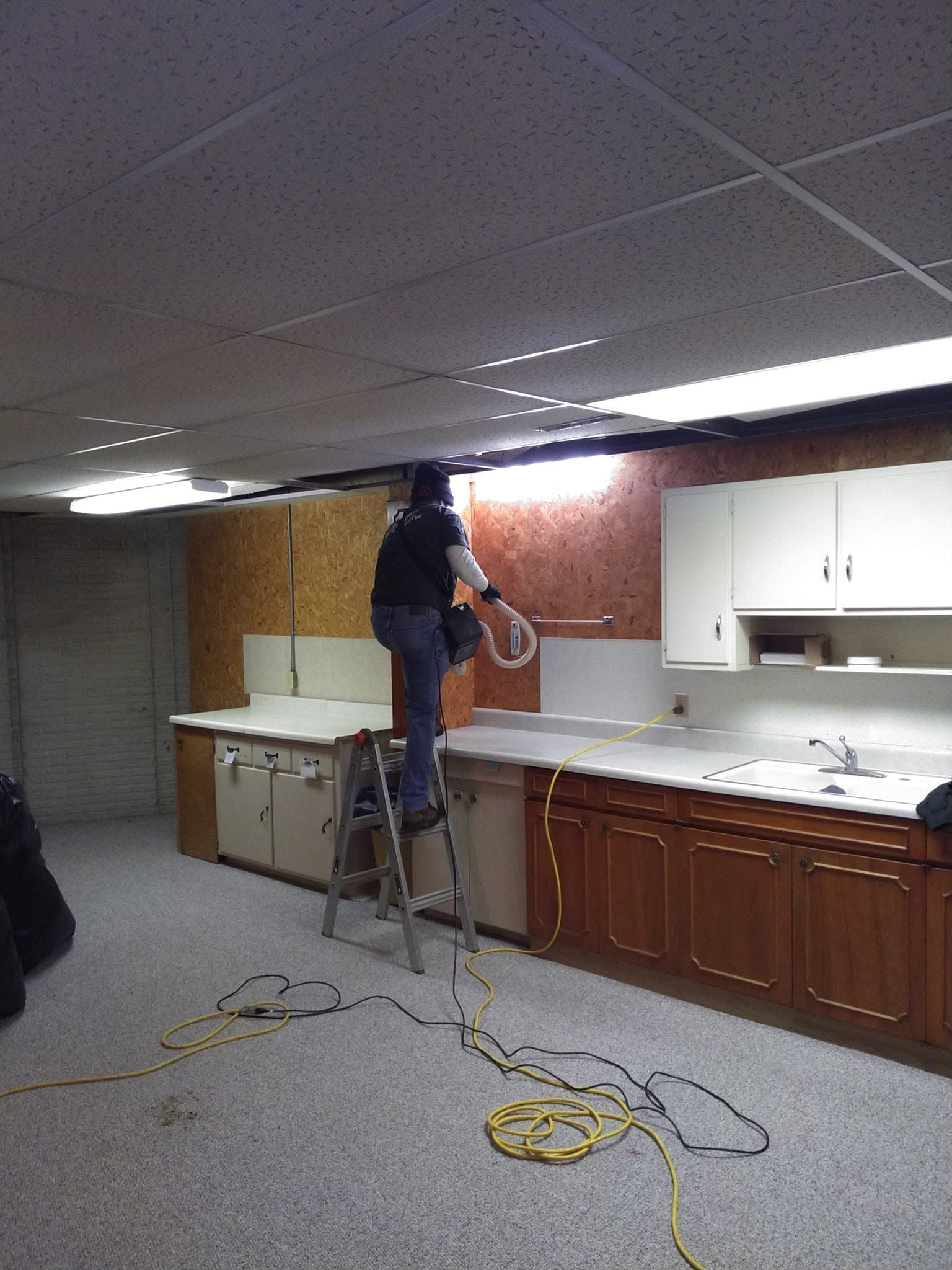 Person on a ladder working above a kitchen counter in a room with cabinets and cords on the floor