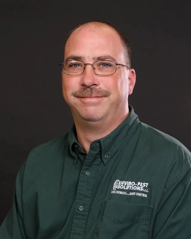 Portrait of a smiling man in glasses and a green button-up shirt against a dark background