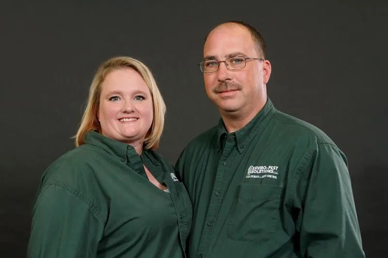 Two people in green collared shirts posing against a dark gray background.