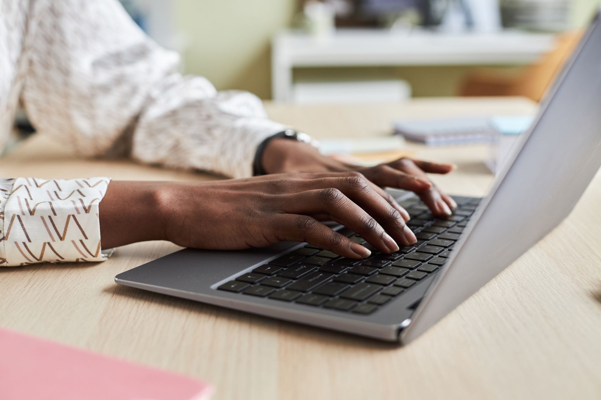 Hands typing on a laptop at a desk in a bright office