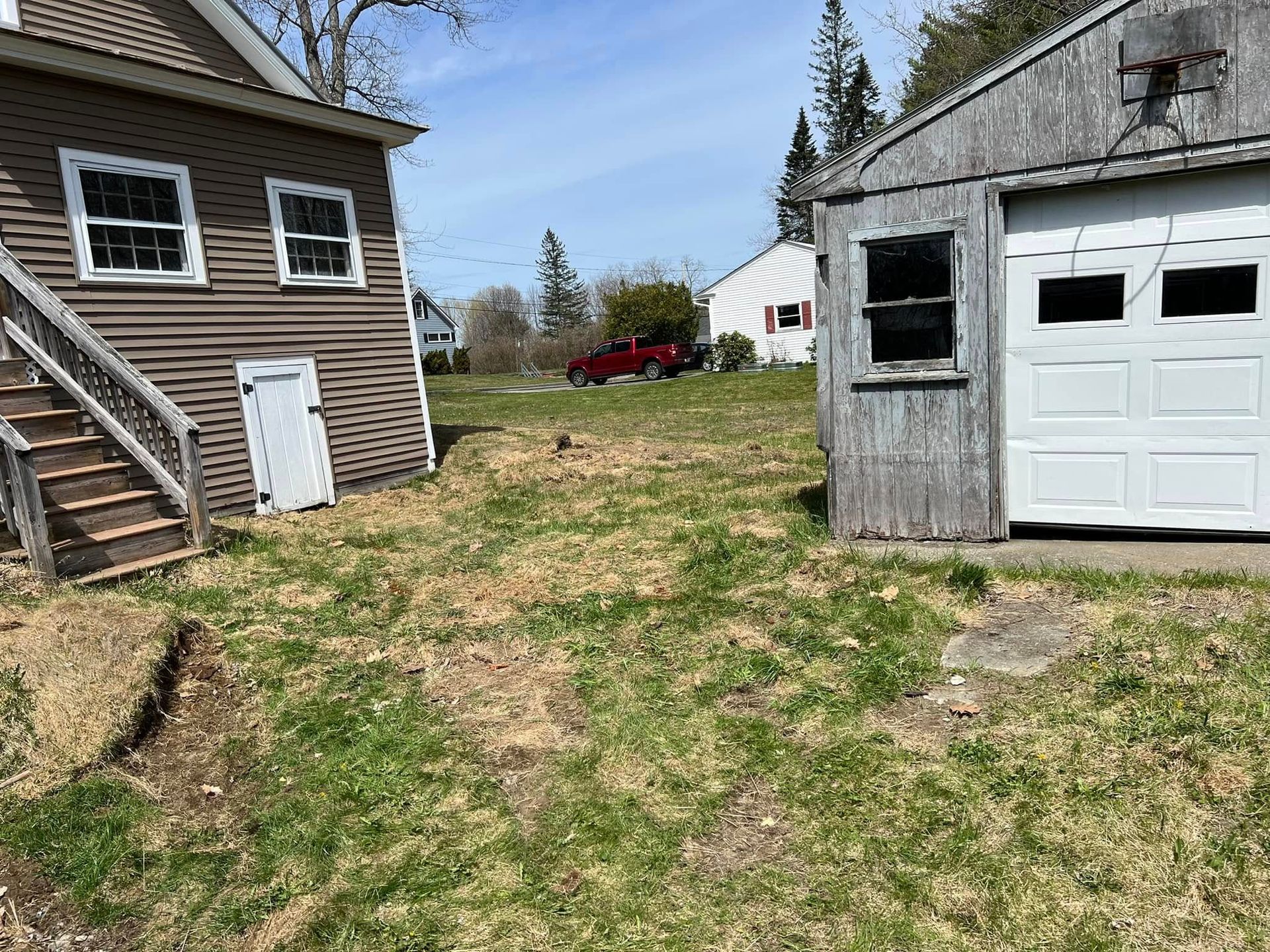 Backyard between two houses with a patchy lawn and a white garage door on the right