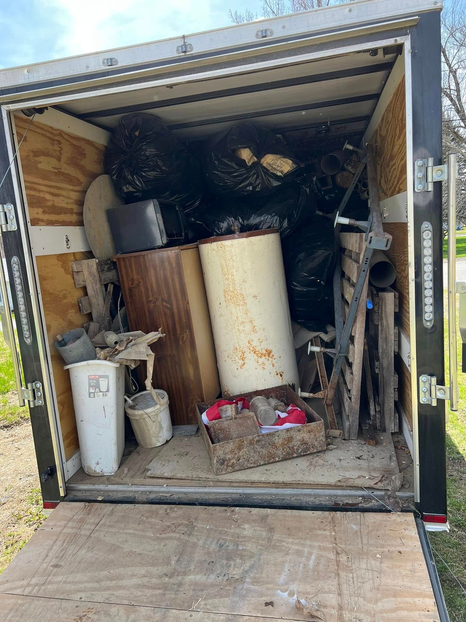 Open trailer packed with clutter, including a water heater, buckets, and tools.
