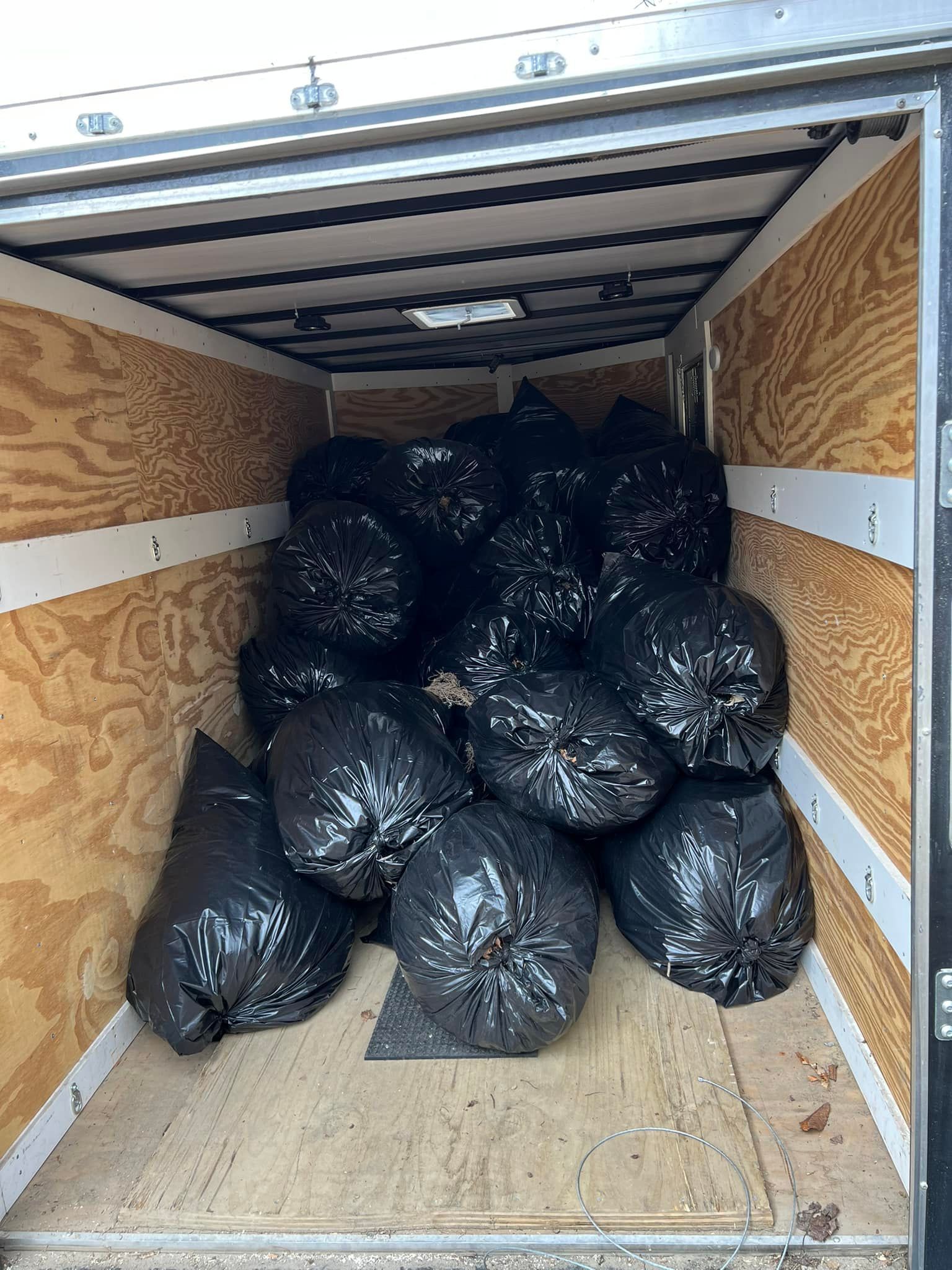 Large trailer interior filled with piled black trash bags on a wooden floor