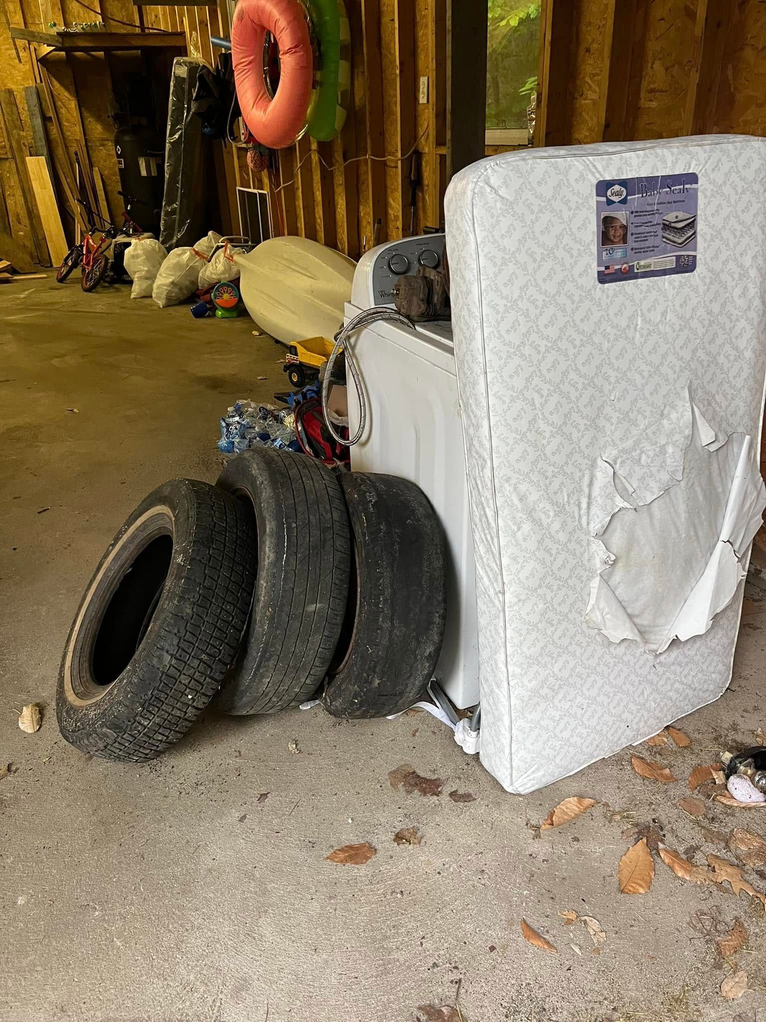 Discarded tires beside a damaged white appliance in a cluttered alley or storage area