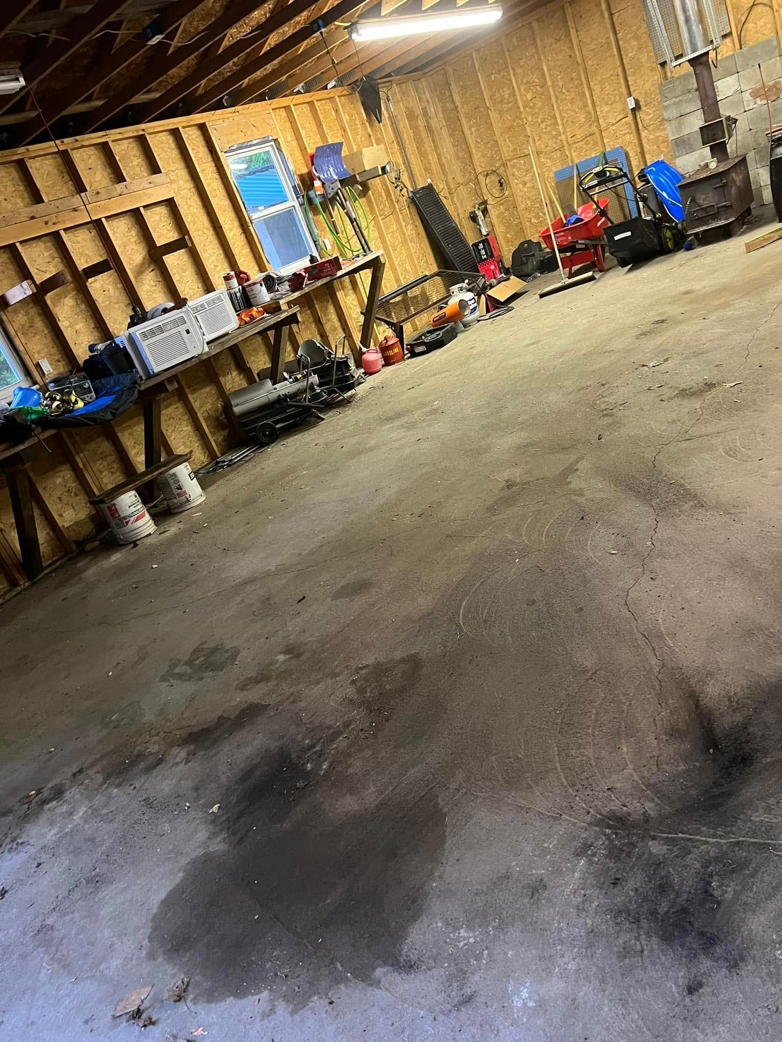 Tilted view of a cluttered workshop with tools, bins, and equipment along the walls on a concrete floor.