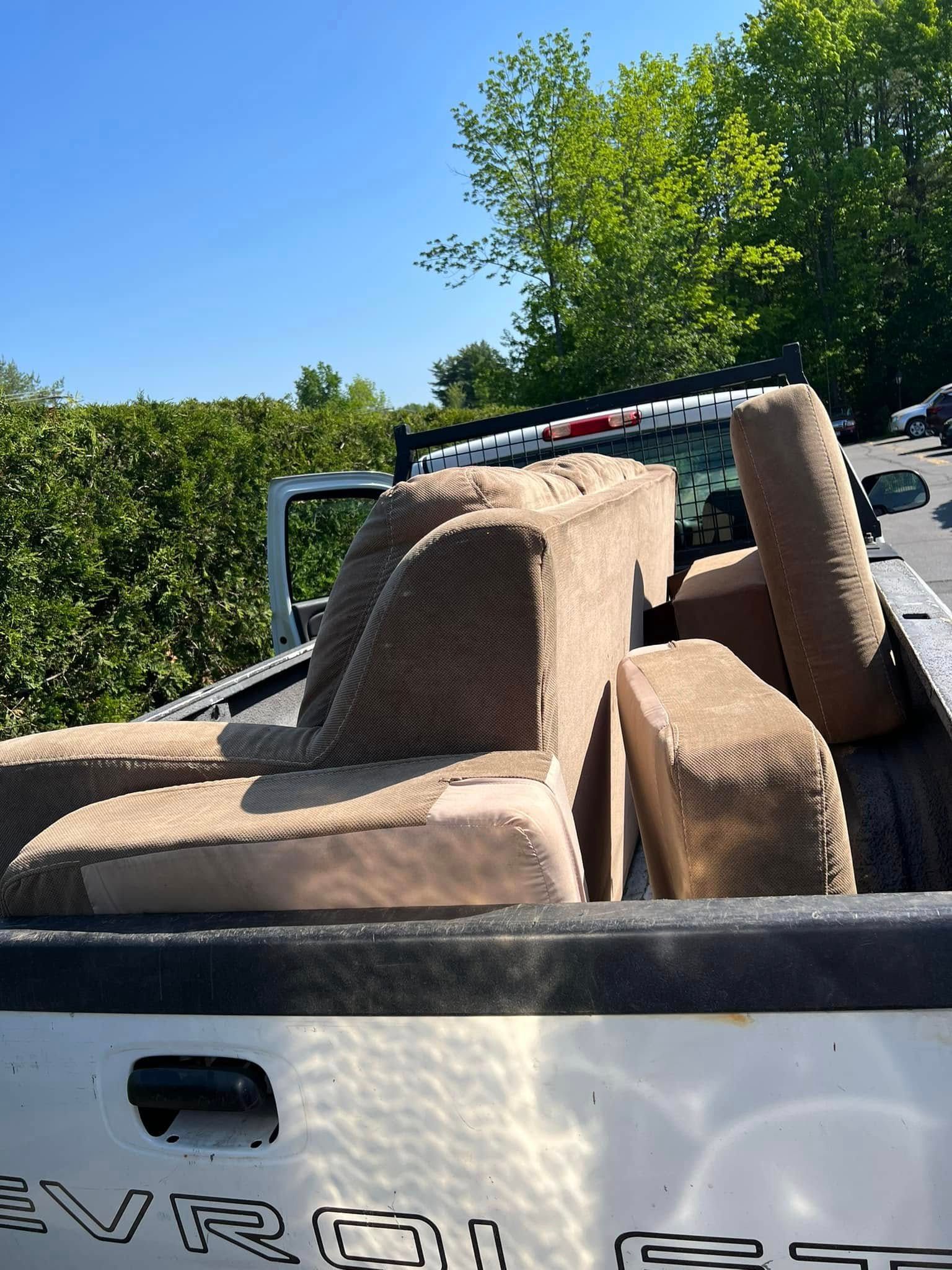 Tan/brown recliner chairs piled in the back of a white Chevrolet truck outdoors under a blue sky