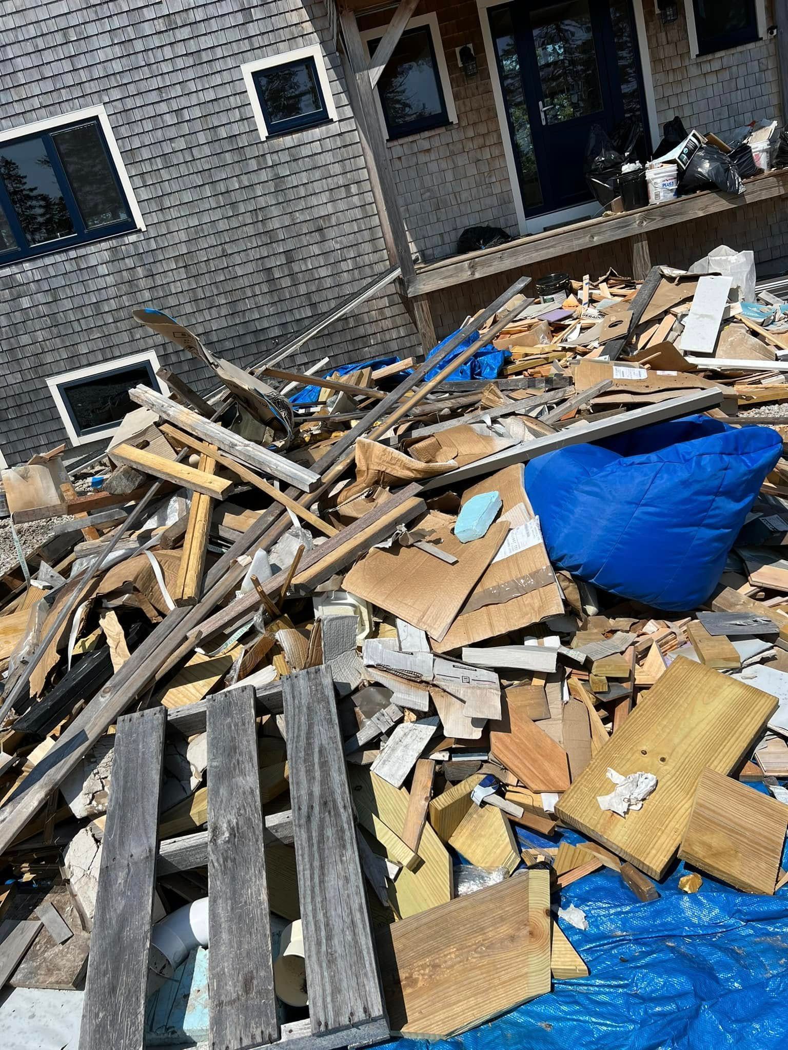 Demolition debris piled beside a brick building, with wood scraps and a blue tarp.